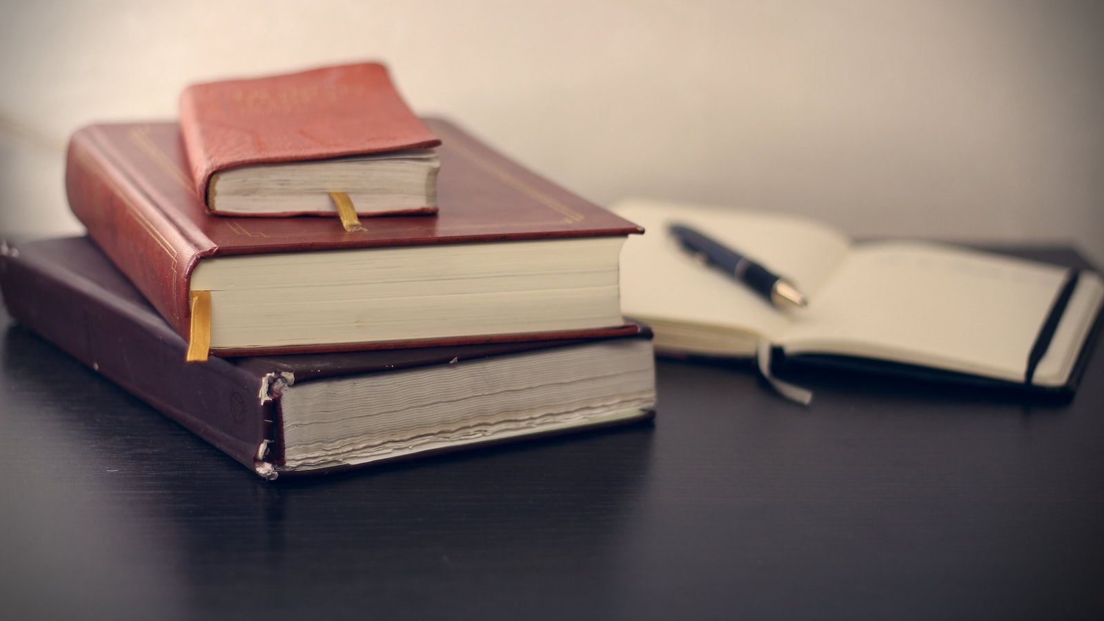 Selective focus photography of three books beside opened notebook with a pen.