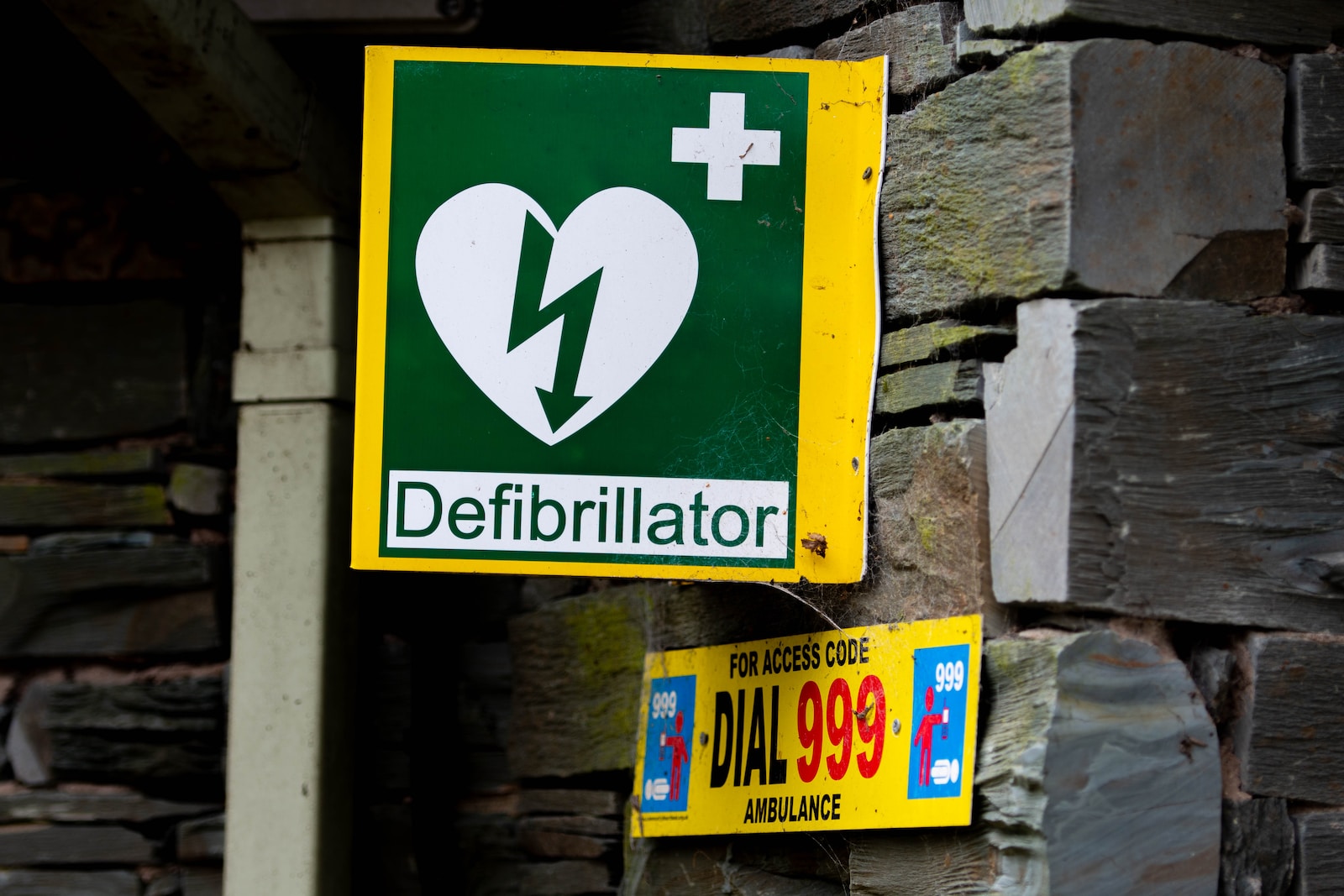 A green and yellow sign with a heart on it which says "Defibrillator"