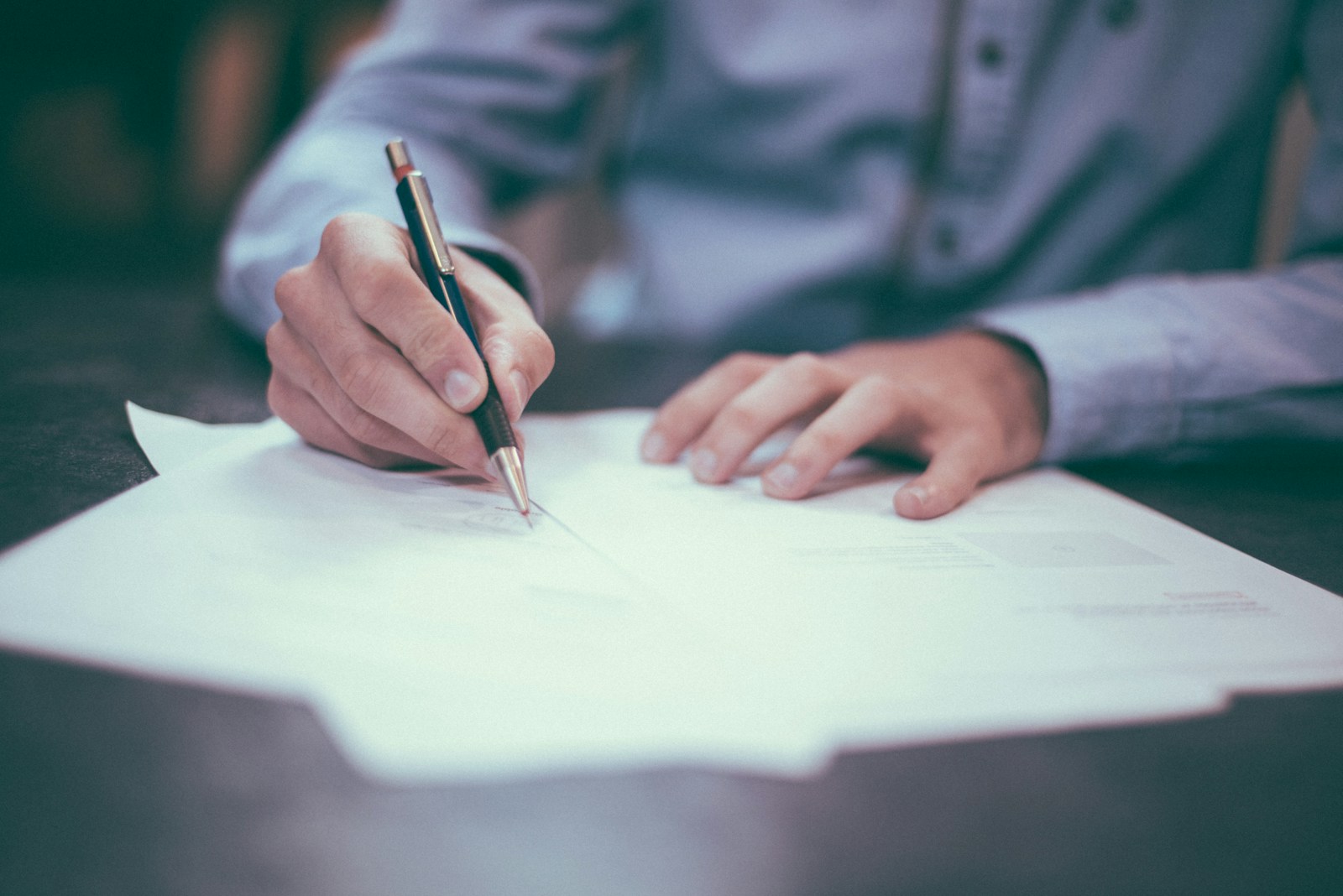 Person signing a contract on table.