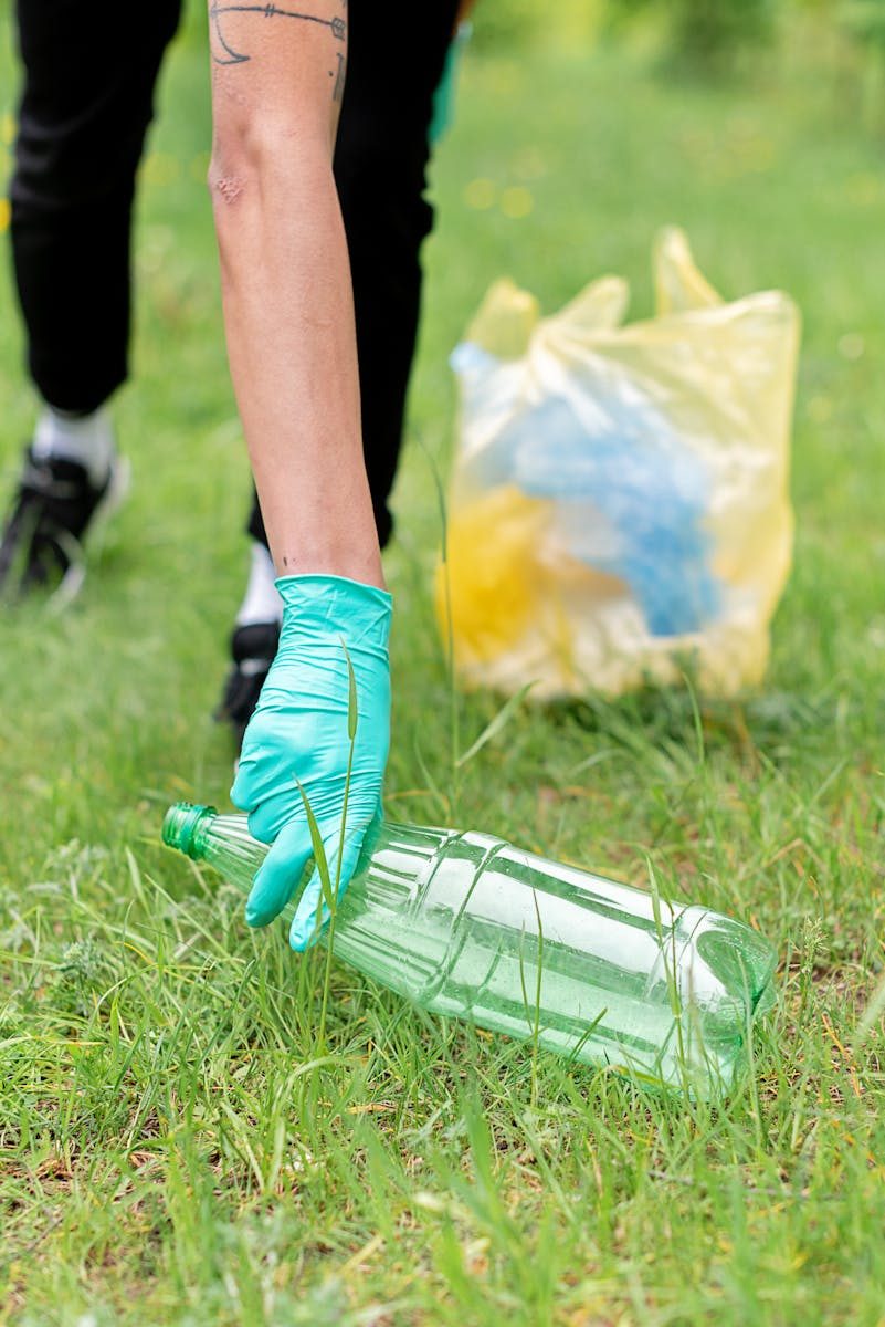 Close-up of a person wearing gloves collecting litter in a grassy area, promoting recycling.